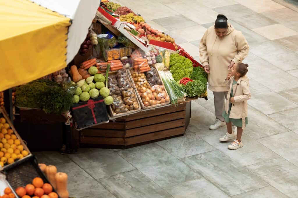 Mother and daughter near a vegetable stall in the concept of 'best local shops and markets in Bromley for new residents'.