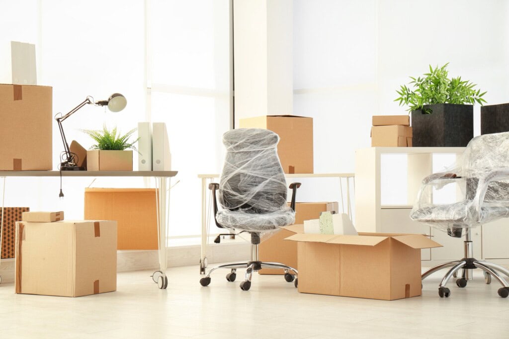 Moving boxes and office furniture in the concept of 'How to communicate an office move to clients and partners'.
