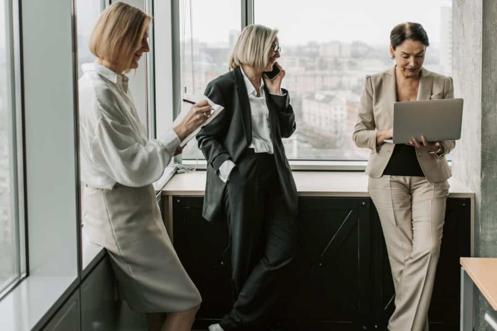 Female employees at the corner of a conference room doing work while waiting for the meeting to begin in the concept of 'How to Minimise Disruption During an Office Move'.