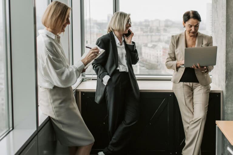 Female employees at the corner of a conference room doing work while waiting for the meeting to begin in the concept of 'How to Minimise Disruption During an Office Move'.